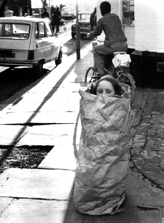 Black & white photograph. Girl playing in paper bag